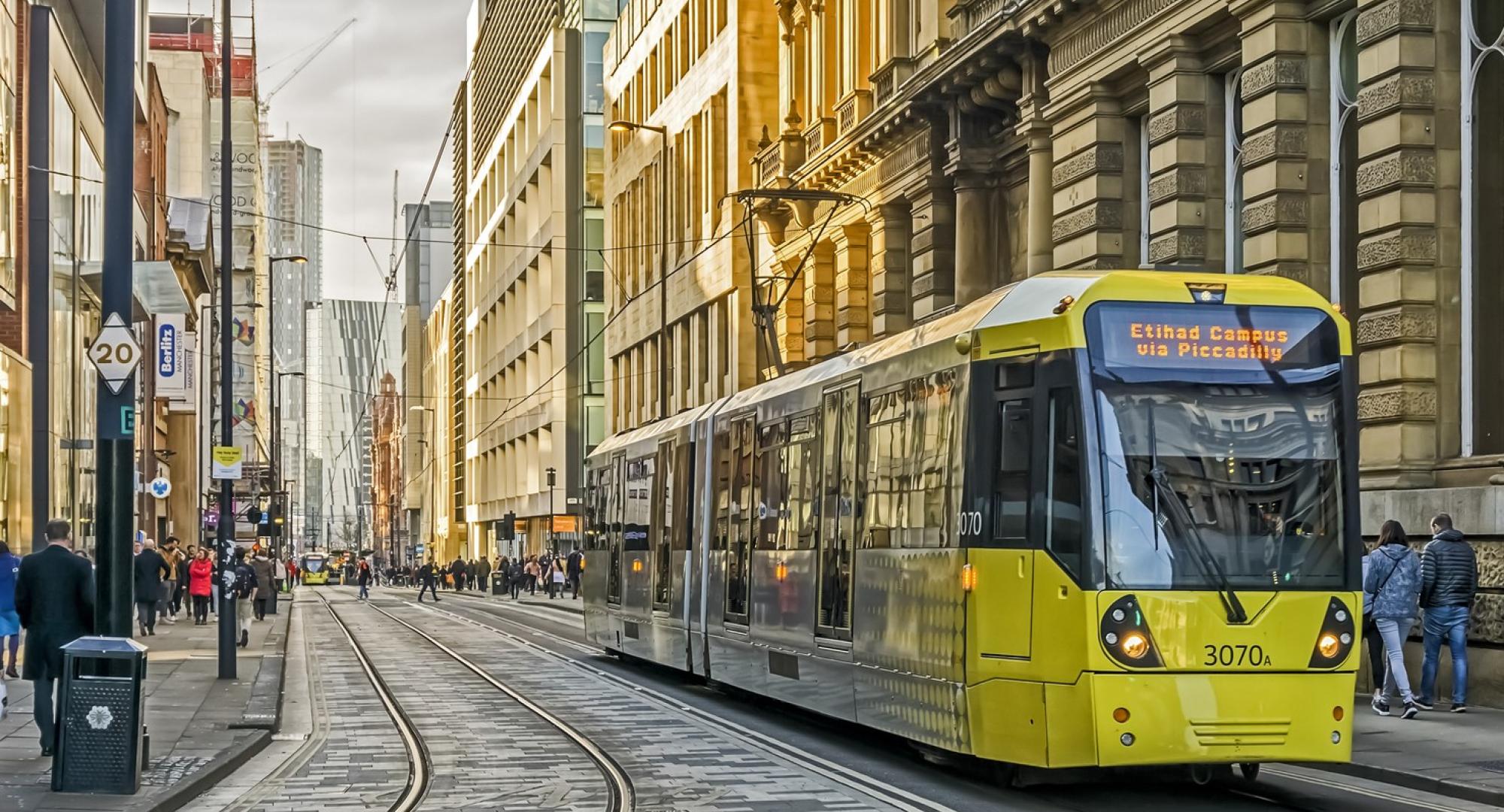 View of Manchester city centre, UK. A tram can be seen approaching and people can be seen walking on the roads.