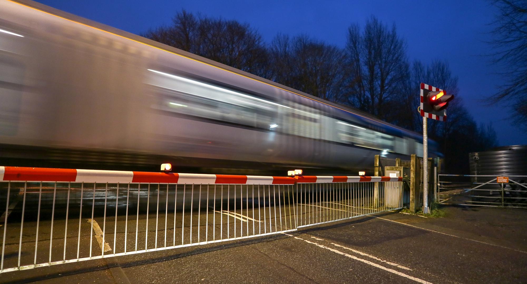 Warning lights showing and the barriers down at a level crossing as a train speeds past, via Istock 